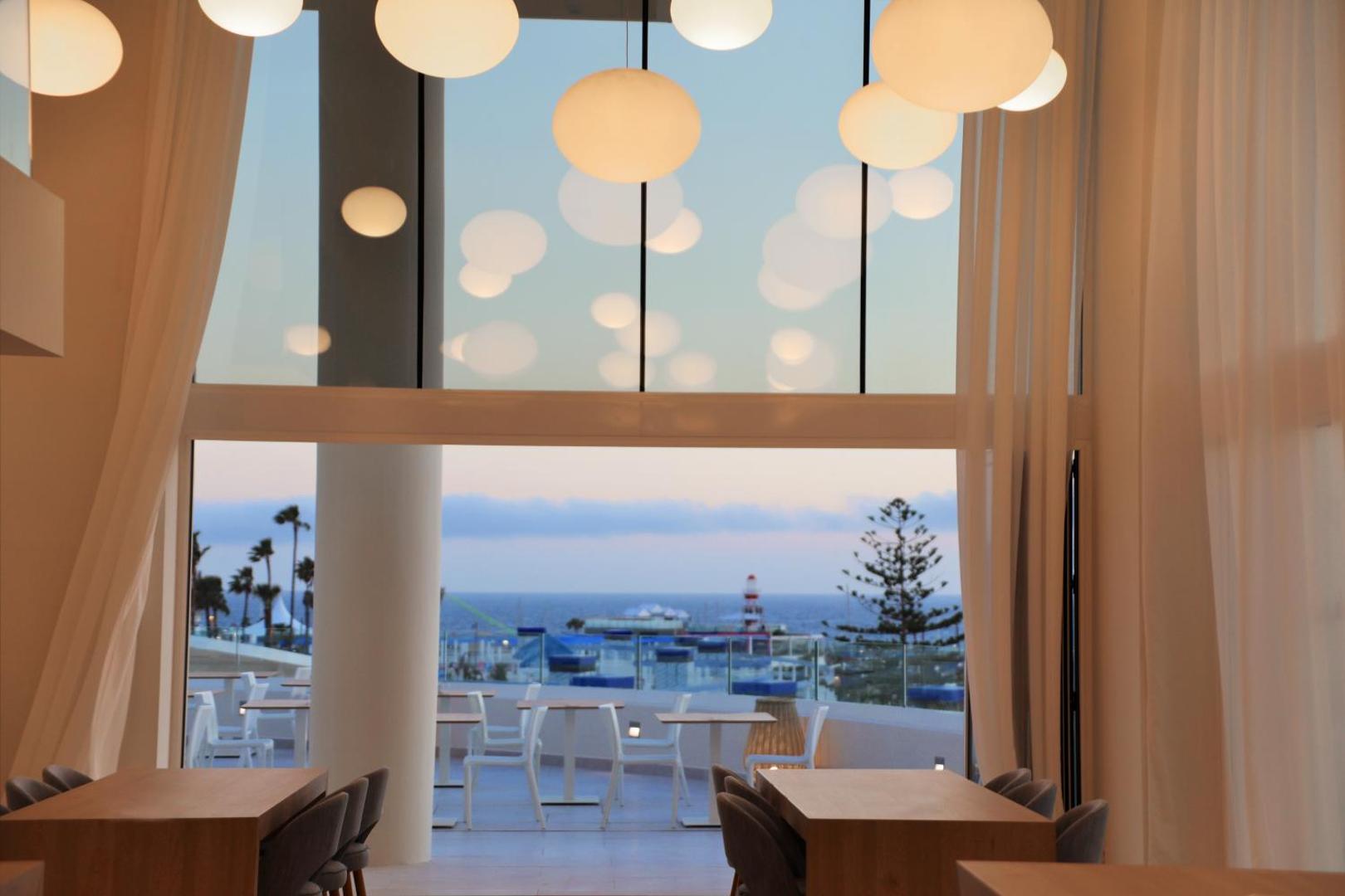 Skats no Iberostar Sabila restorāna terases uz okeānu saulrietā — moderns apgaismojums un panorāmas logi Tenerifes piekrastē