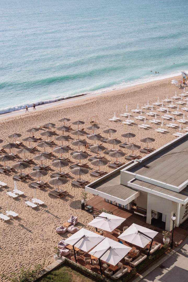 Skats no augšas uz Grifid Encanto Beach privāto pludmali ar saulessargiem, zviļņiem un pludmales restorānu Zelta smiltīs