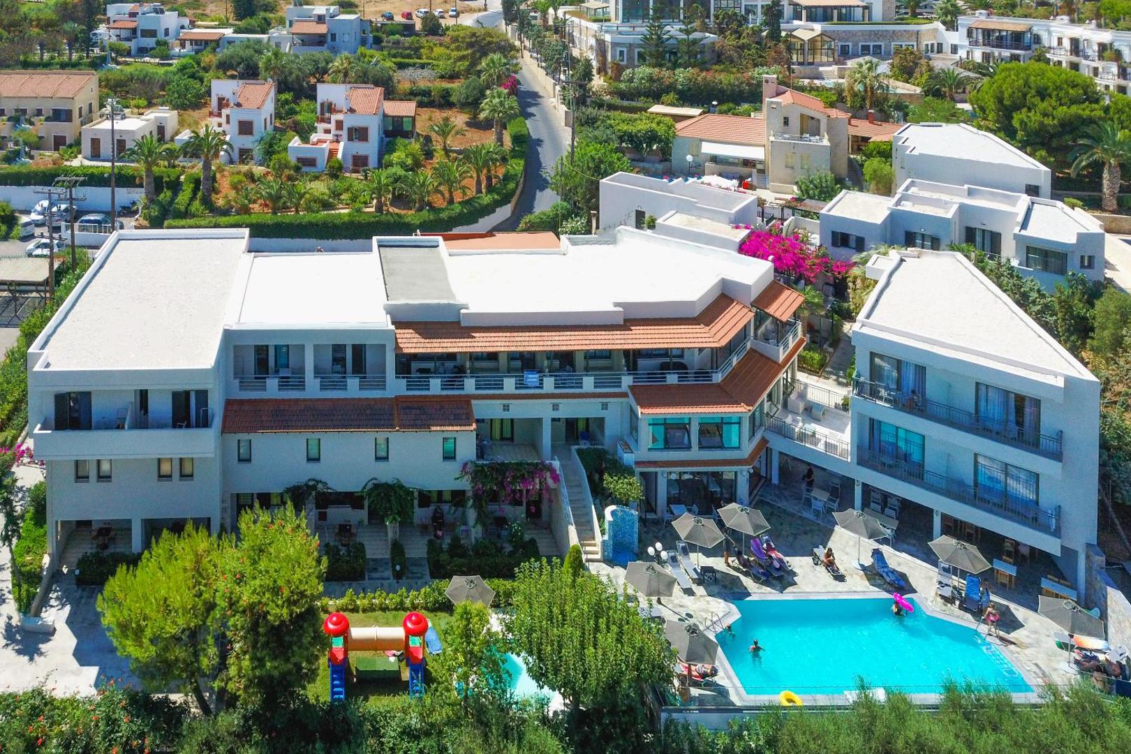Anna Maria Village viesnīcas ēkas un āra baseins Anisarā, Krētā — skats no augšas uz kūrorta teritoriju un bērnu rotaļu laukumu
