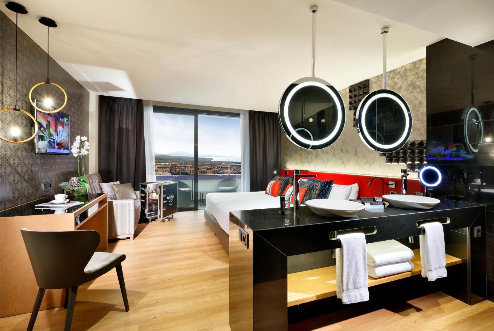 Hard Rock Hotel Tenerife dizaina numura interjers ar atvērtā plānojuma vannasistabu, modernām izlietnēm un skatu uz pilsētu.
