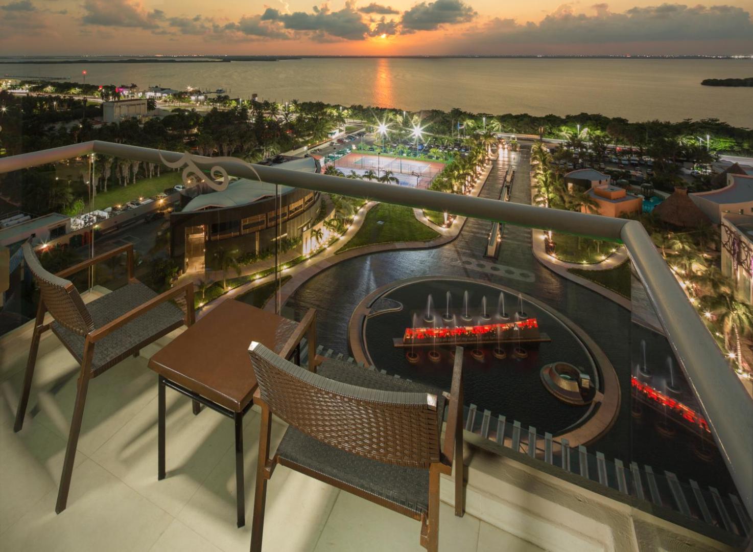Skats no Hard Rock Hotel Cancun numura balkona uz viesnīcas teritoriju, strūklakām un lagūnu saulrieta laikā