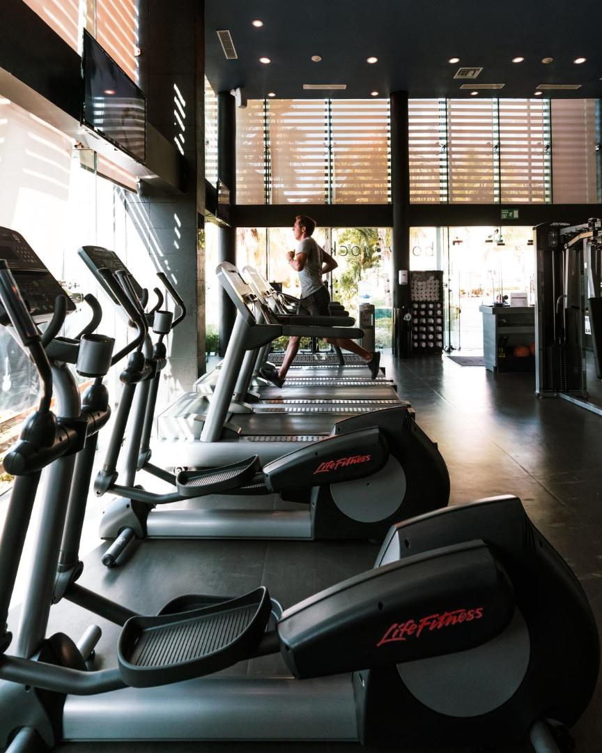 Hard Rock Hotel Cancun fitnesa centrs ar skrejceliņiem un eliptiskajiem trenažieriem, kur viesi sporto pie lieliem logiem ar skatu uz Kankunu