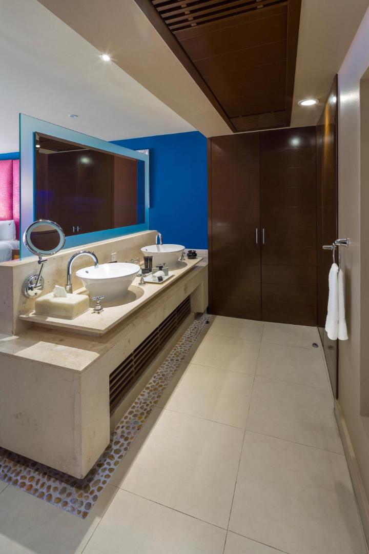 Hard Rock Hotel Cancun numura vannas istaba ar divām izlietnēm, lielu spoguli un modernu dizainu zilā un brūnā krāsā
