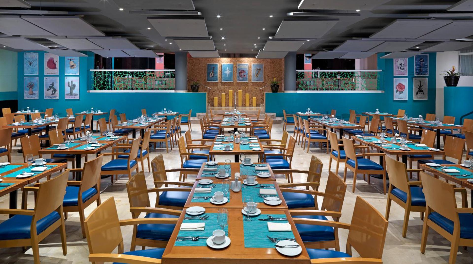 Hard Rock Hotel Cancun plašā galvenā restorāna zāle ar ziliem krēsliem, koka galdiem un modernu sienu dekoru Kankunā