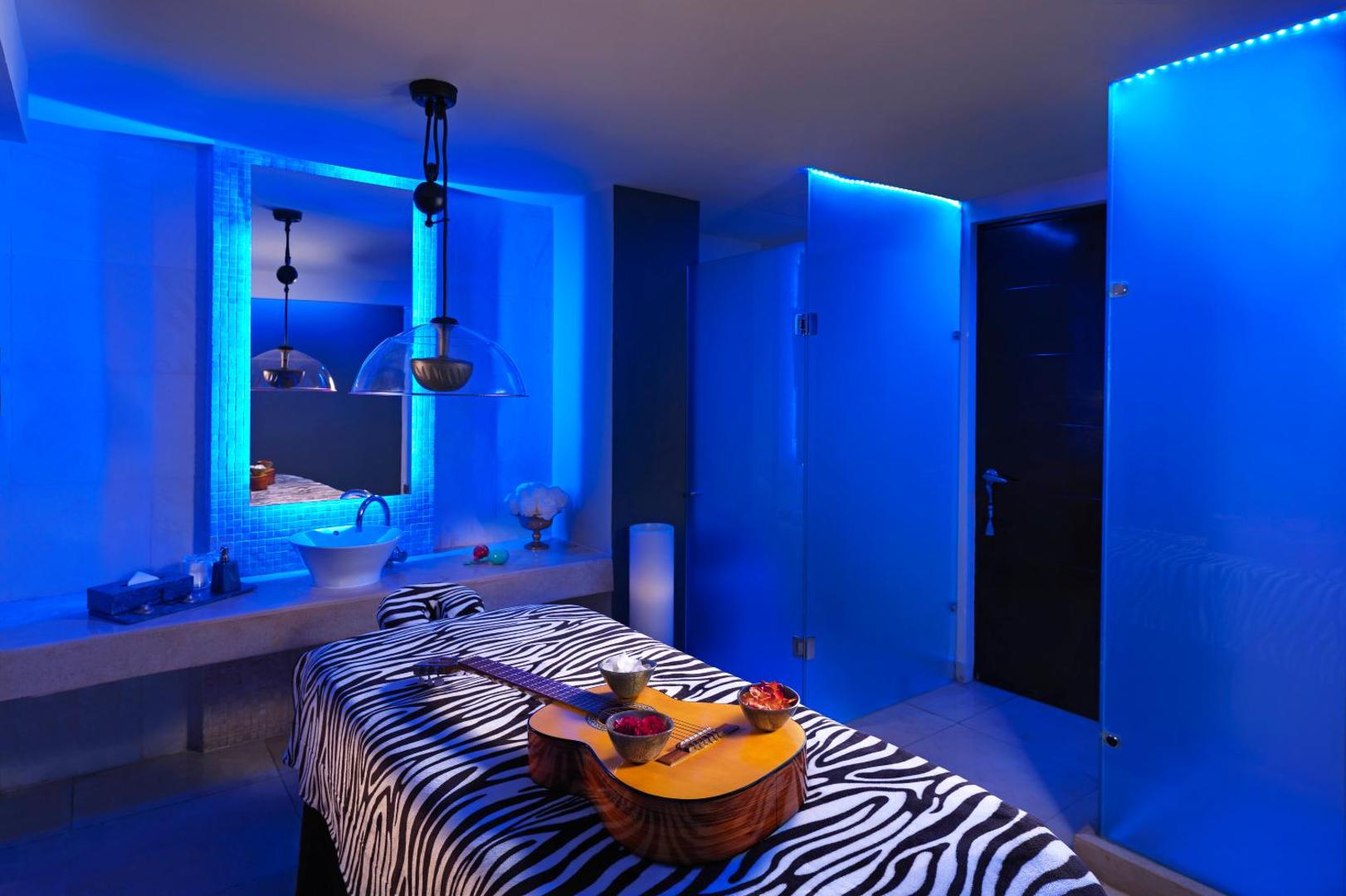 Hard Rock Hotel Cancun spa procedūru numurs ar zilu apgaismojumu, masāžas galdu un dekoratīvu ģitāru rokstila gaisotnē