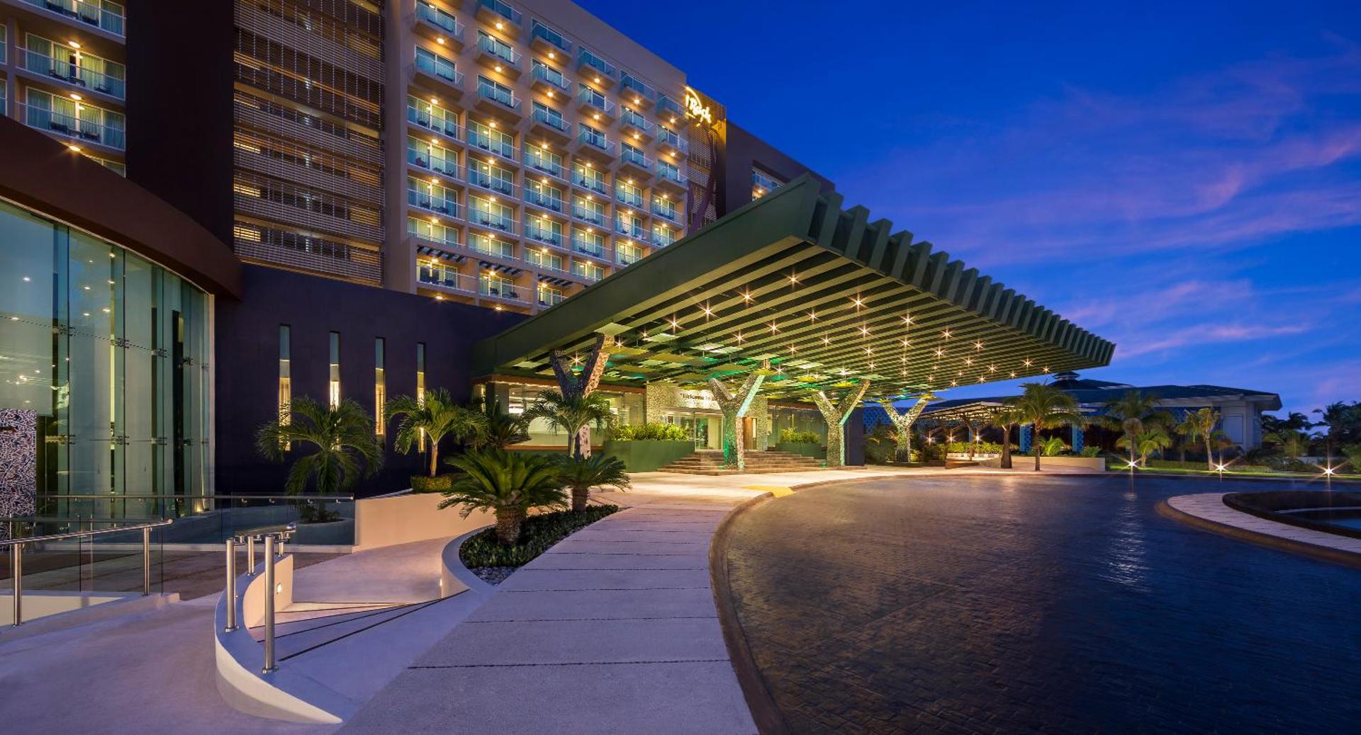 Hard Rock Hotel Cancun modernā ieejas nojume ar zvaigžņotu apgaismojumu un palmu dārzu vakarā Kankunas kūrortā
