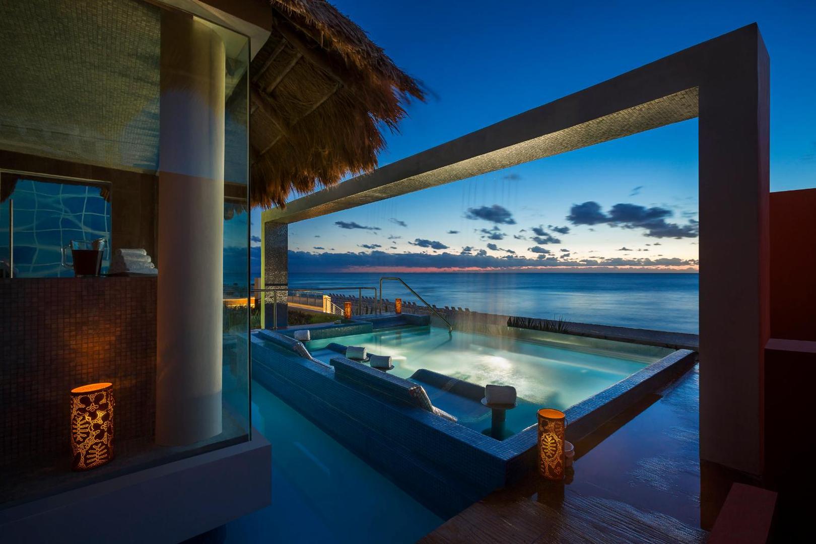 Hard Rock Hotel Cancun āra džakuzi baseins piekrastē saulrieta laikā ar skatu uz Karību jūru un dekoratīvām laternām