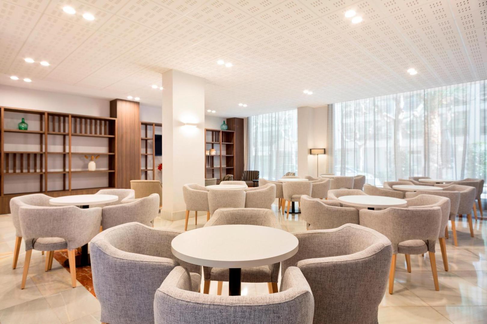 Best Da Vinci viesnīcas lobby bārs un atpūtas telpa ar pelēkiem atpūtas krēsliem, apaļiem galdiņiem un koka plauktiem
