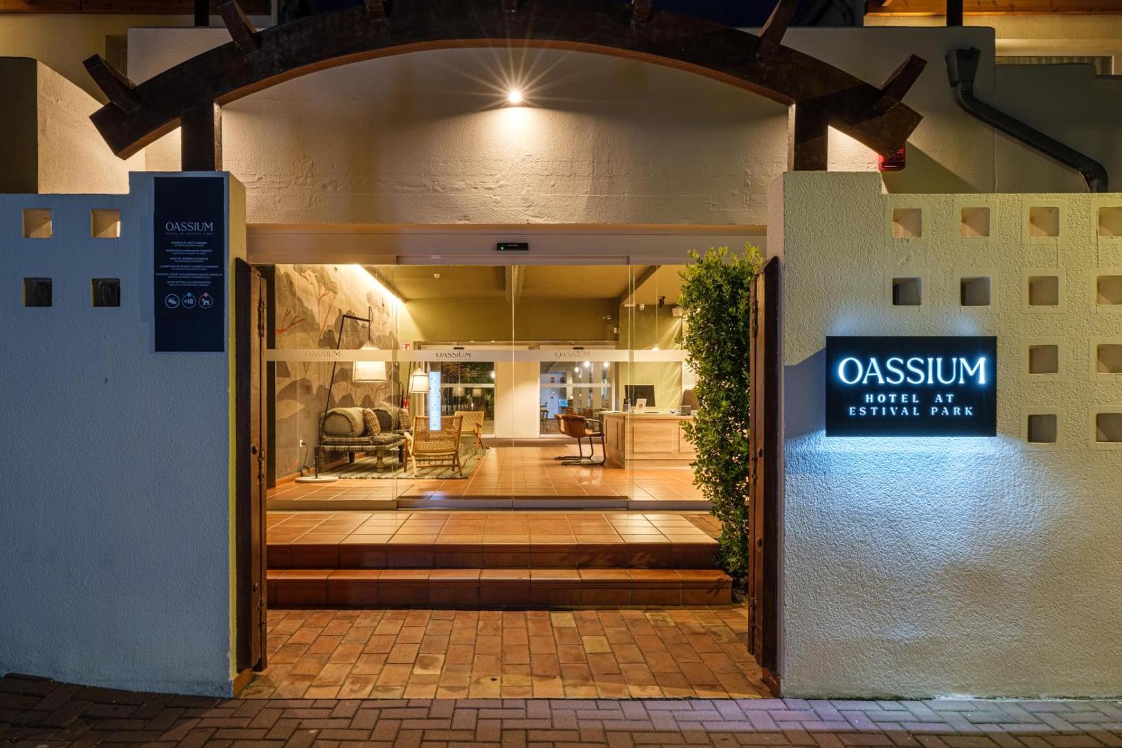 Oassium Hotel at Estival Park ieeja vakarā — izgaismota viesnīcas izkārtne un mājīgs vestibils ar dīvāniem La Pinedā, Spānijā