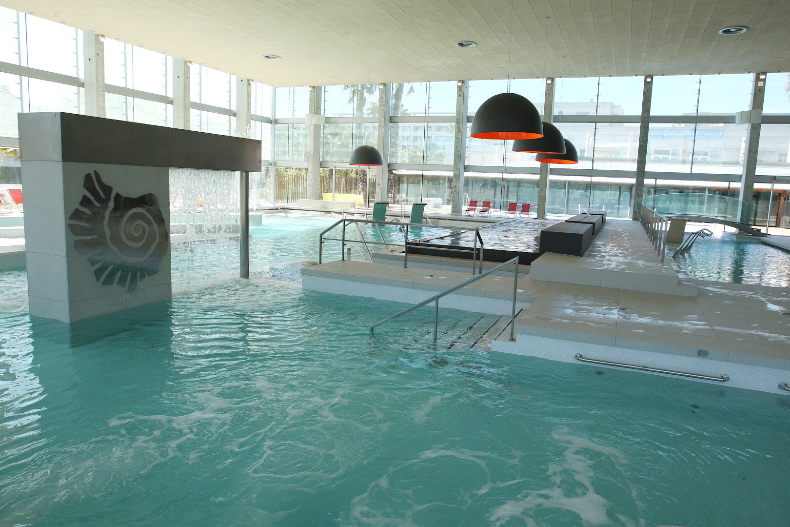 Plašs Oassium Hotel iekštelpu spa komplekss ar lielu baseinu, kaskādēm un panorāmas logiem, kas sniedz daudz dabiskās gaismas.