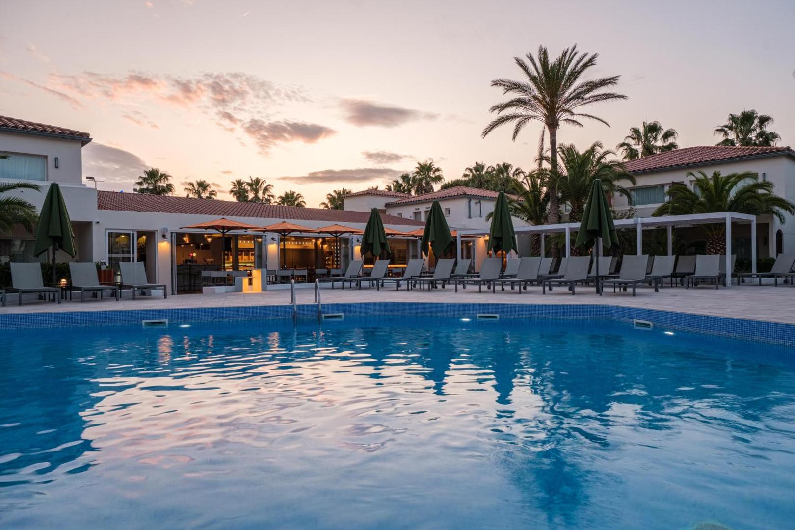 Oassium Hotel - Adults Only baseina zona saulrieta laikā ar izgaismotu terasi un vakariņu zonu fonā