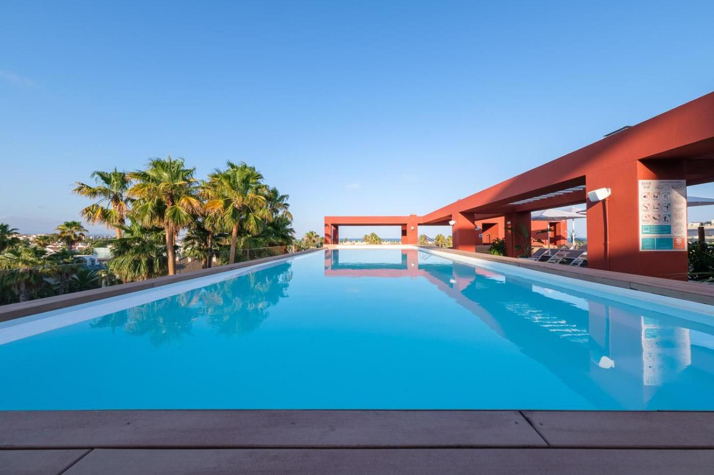 Oassium Hotel - Adults Only baseins ar pārplūdes malu uz jumta terases, no kuras paveras skats uz palmām