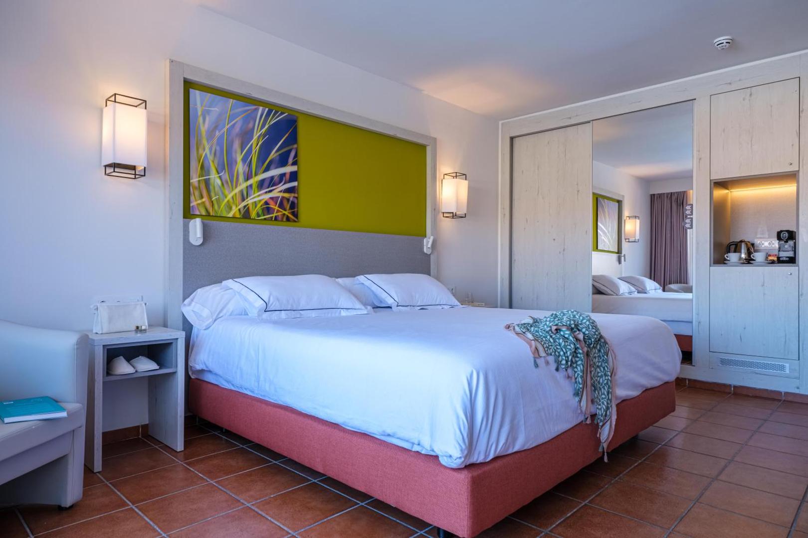 Oassium Hotel numura interjers ar iebūvētu skapi, spoguli, kafijas stūrīti un ērtu divvietīgu gultu gaišos toņos.