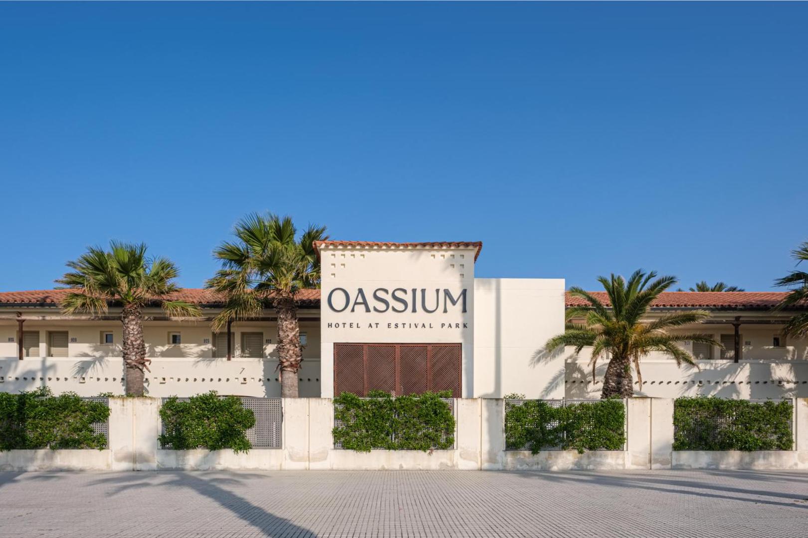Oassium Hotel galvenā ēka dienas gaismā — balta fasāde ar palmām un koptu teritoriju La Pinedas kūrortā, Spānijā
