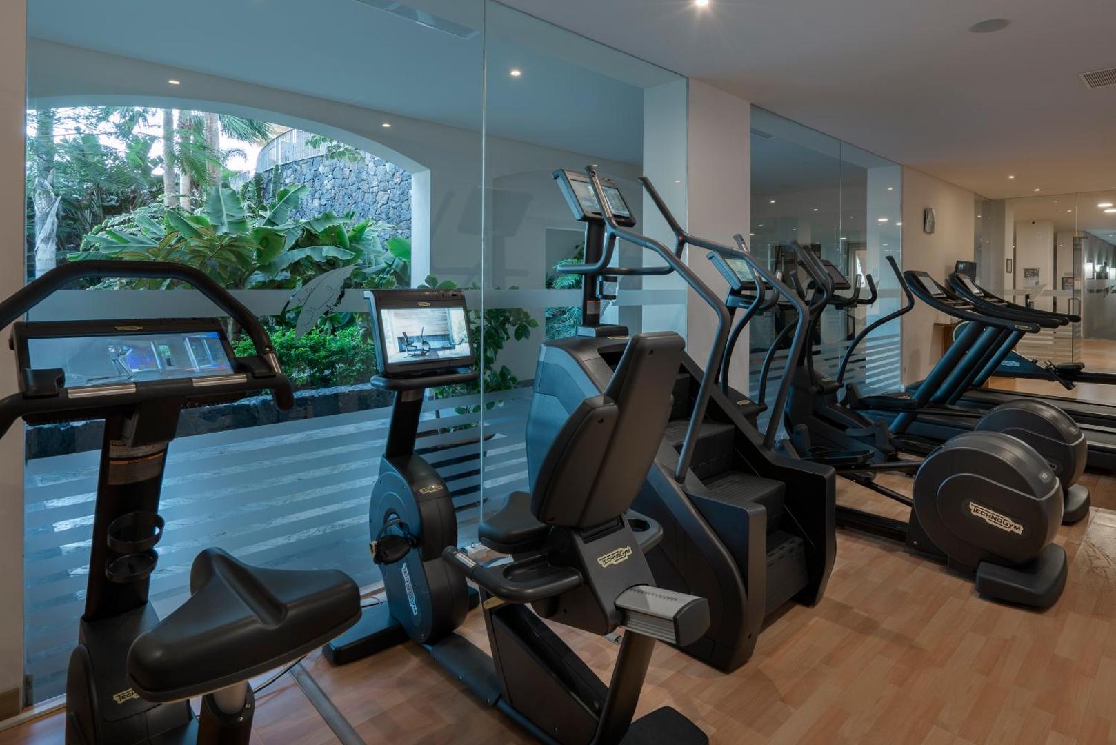Vincci Selección La Plantación del Sur modernā trenažieru zāle ar Technogym kardio aprīkojumu un skatu uz dārzu caur lieliem logiem