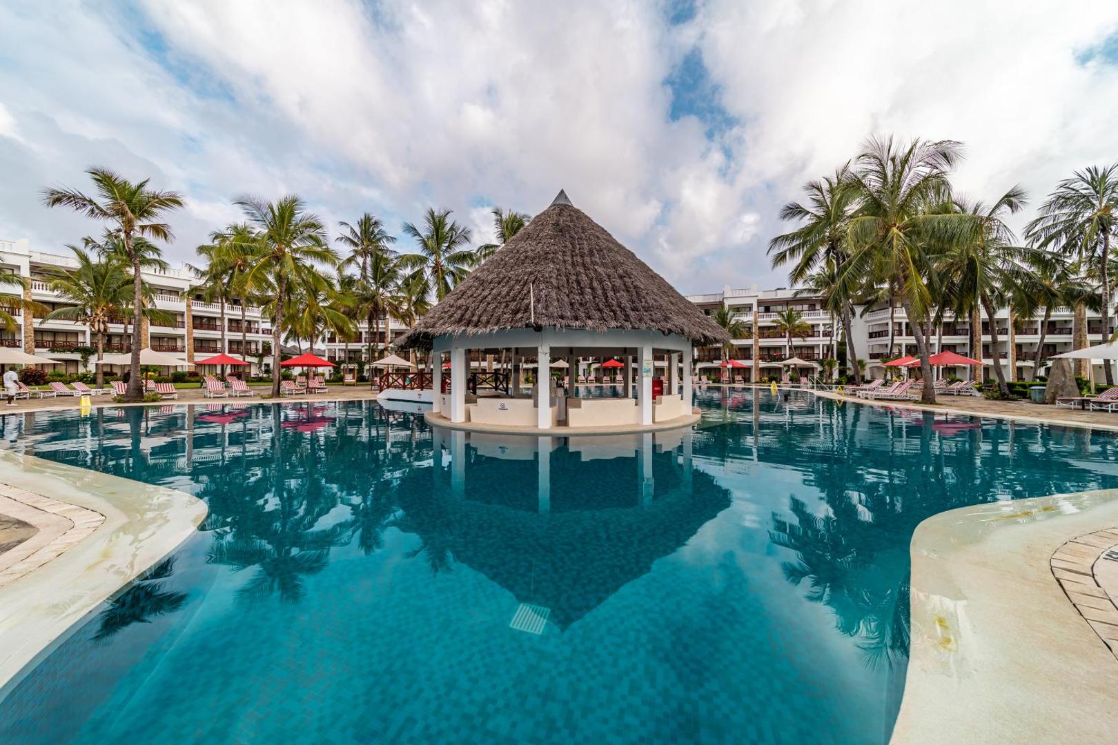 PrideInn Paradise Beach Resort & Spa Mombasa lielais āra baseins ar bāru centrā, palmām un viesnīcas korpusiem fonā