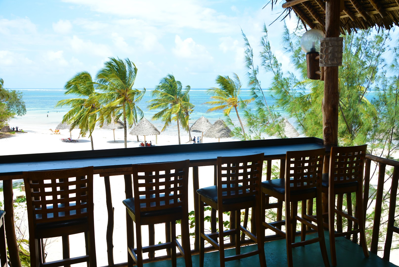 Skats no PrideInn Paradise Beach Resort & Spa Mombasa bāra terases uz balto smilšu pludmali, palmām un Indijas okeānu Kenijā
