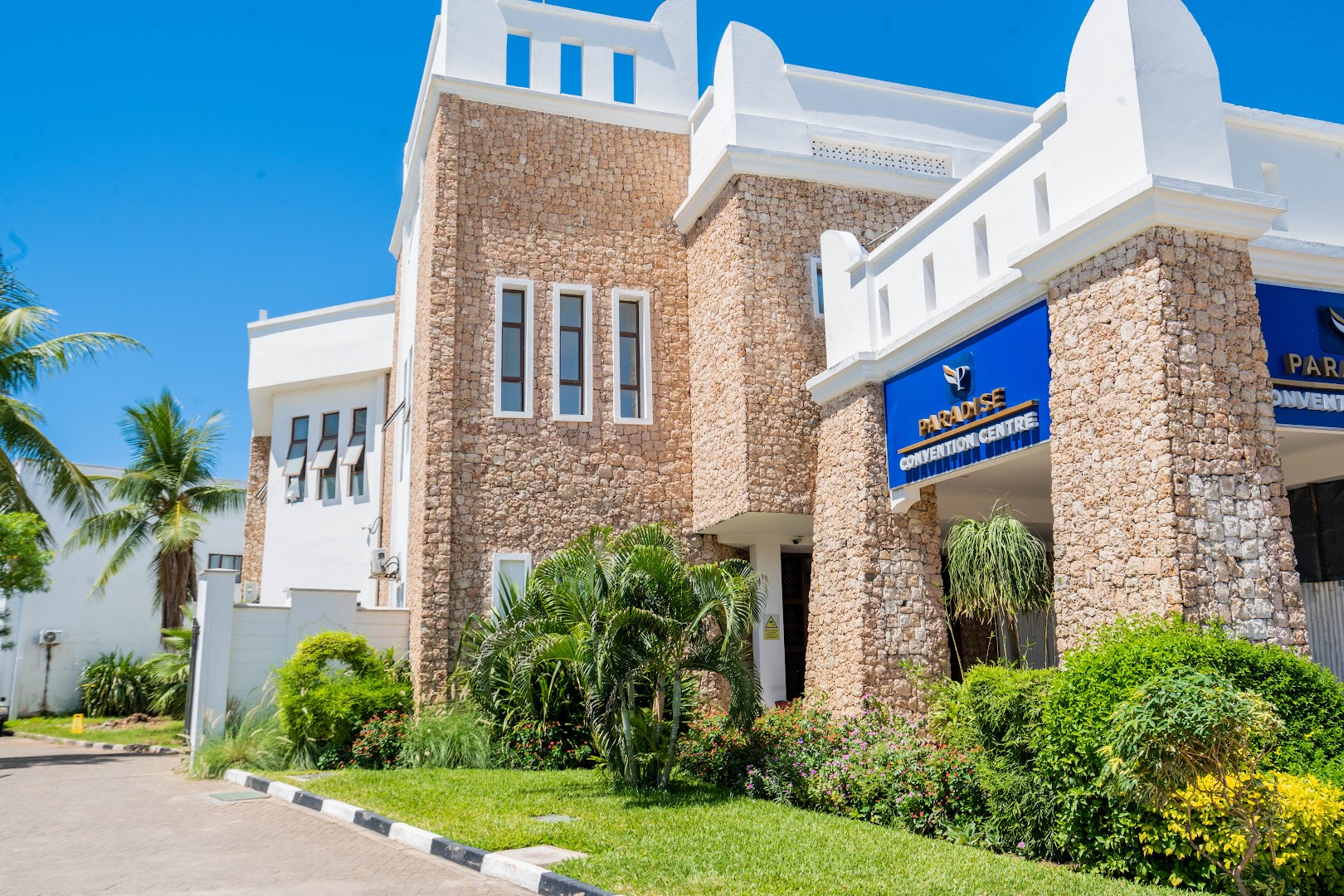 PrideInn Paradise Beach Resort konvenciju centra ēka ar akmens apdari un zilu izkārtni tropu dārza ielokā Kenijas piekrastē