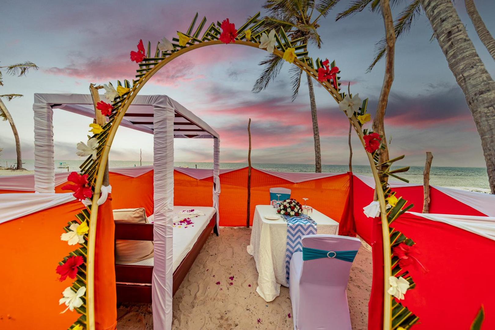 PrideInn Paradise Beach Resort & Spa romantiska vakariņu vieta pludmalē saulrieta laikā ar dekorētu arku un galdiņu smiltīs Mombasā