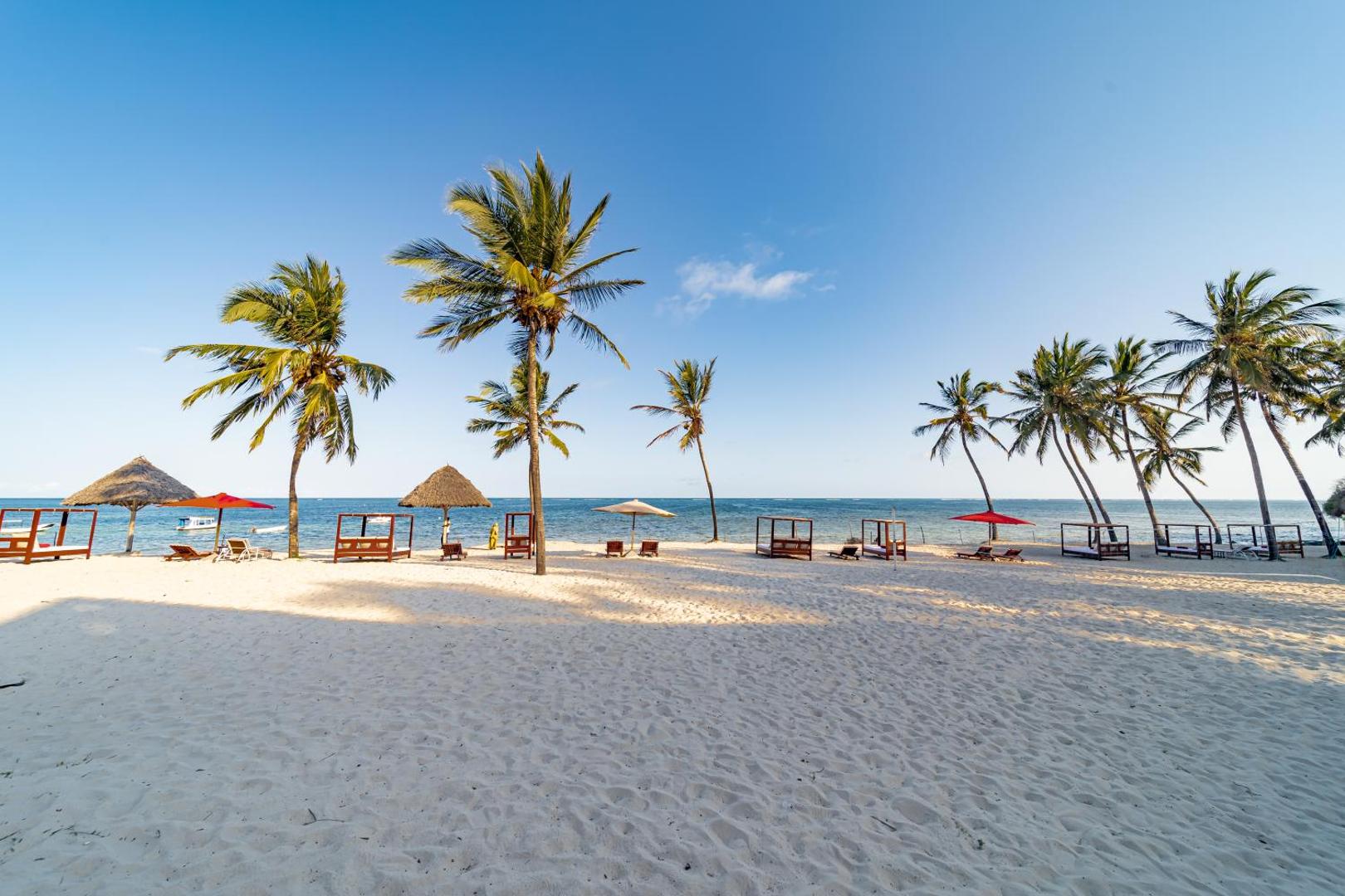 PrideInn Paradise Beach Resort & Spa privātā pludmale Mombasā — balts smilšu krasts, palmas, saulessargi un atpūtas gultas pie okeāna