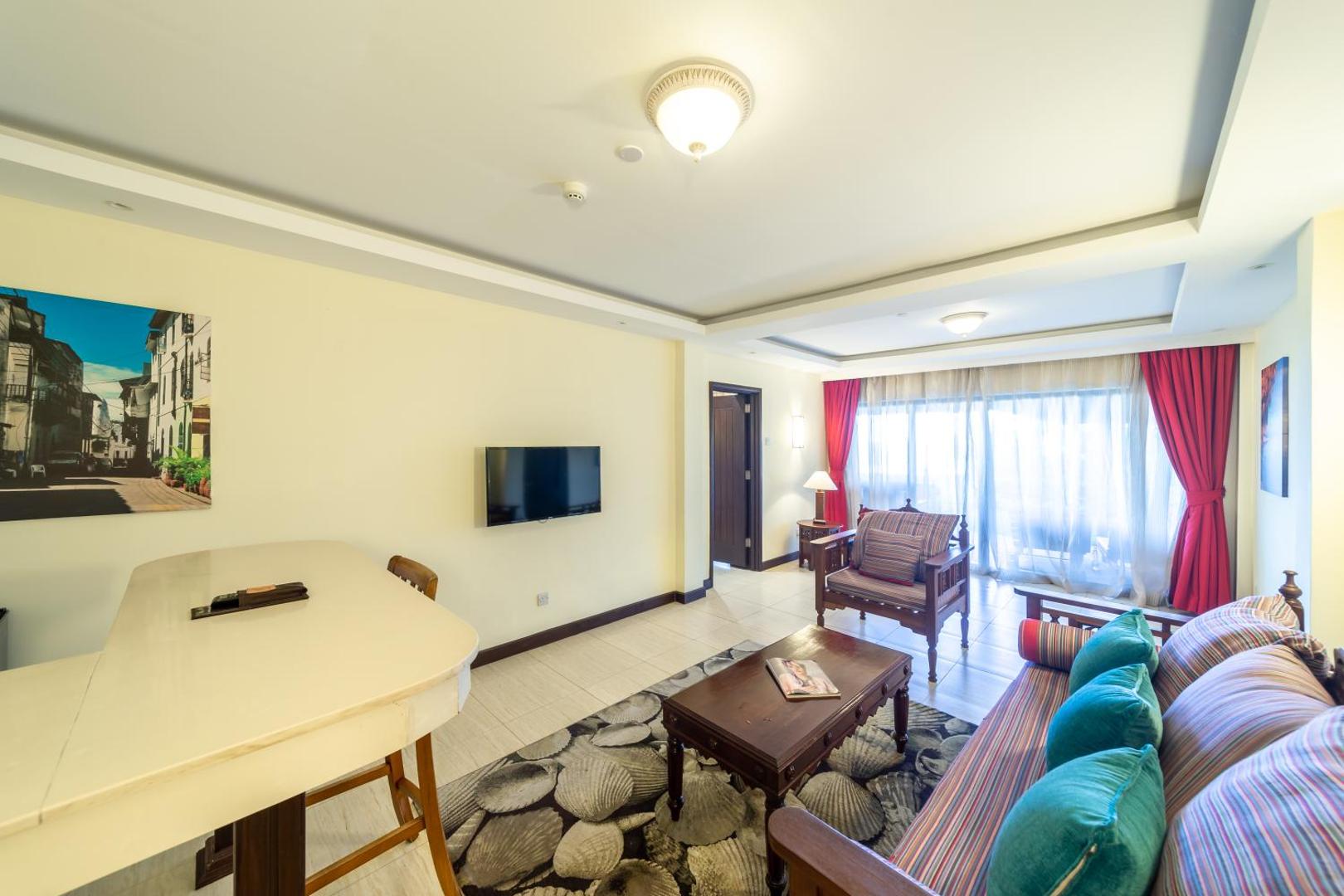 PrideInn Paradise Beach Resort & Spa Mombasa viesnīcas numura dzīvojamā zona ar dīvānu, krēslu un izeju uz balkonu