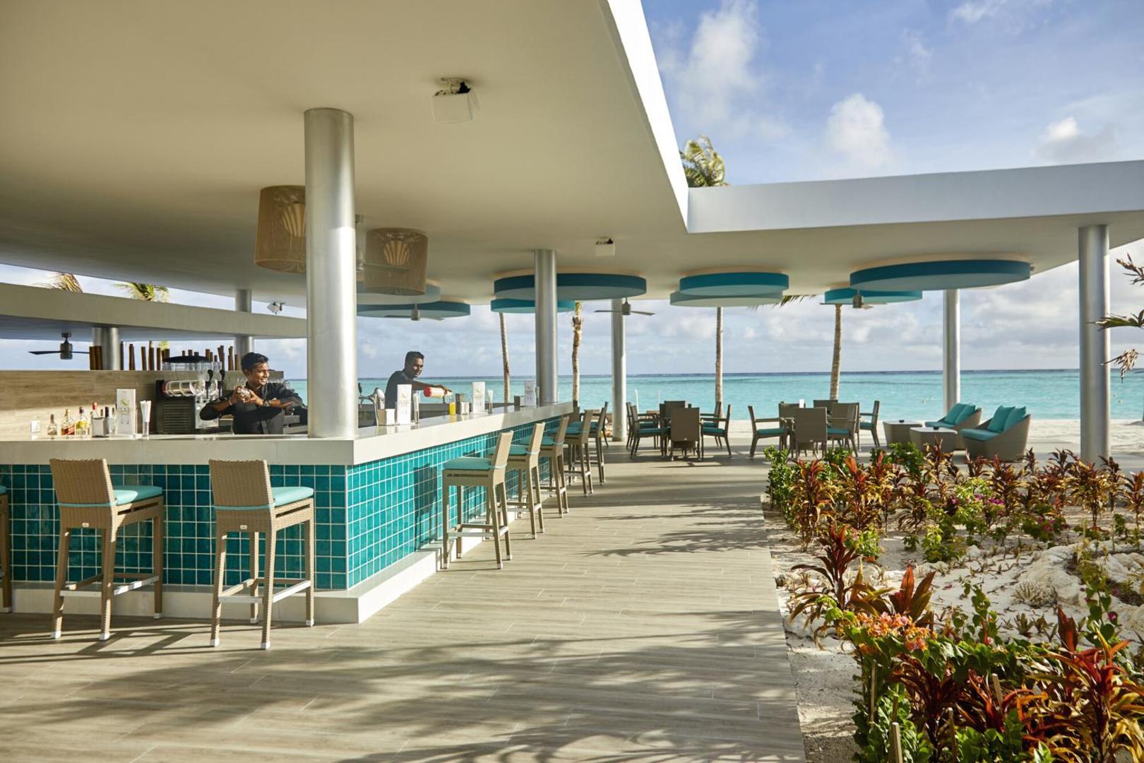 Hotel RIU Atoll pludmales bārs ar tirkīza krāsas flīzēm, bāra krēsliem un skatu uz Indijas okeānu Maldīvās