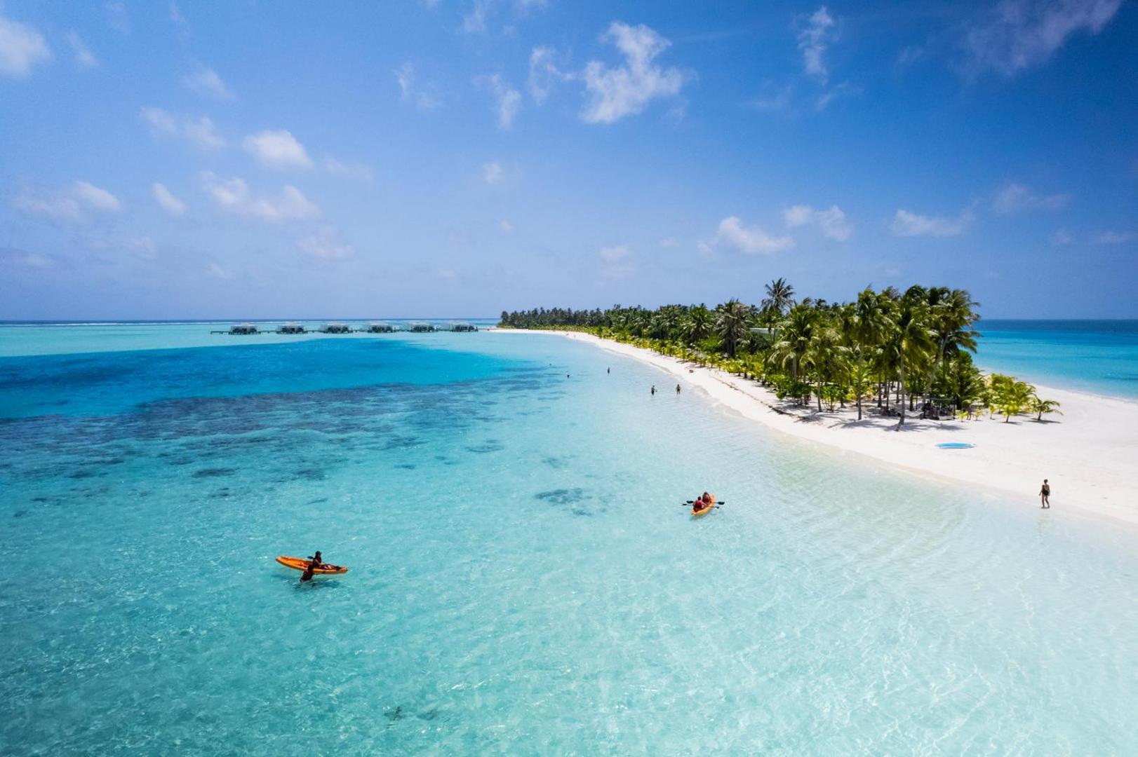 Aerofoto skats uz Hotel RIU Atoll balto smilšu pludmali un tirkīzzilo lagūnu Maldīvijā — atpūtnieki bauda braucienus ar kajakiem