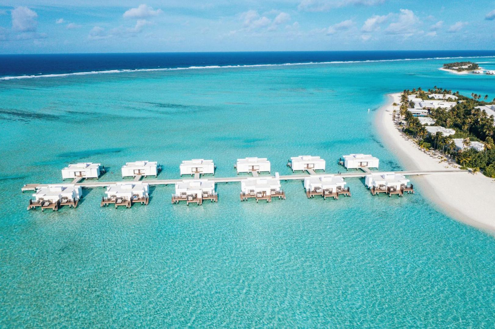 Hotel RIU Atoll ūdens bungalo rinda Maldivu salās — skats no augšas uz modernām baltām mājiņām virs sekla, caurspīdīga ūdens