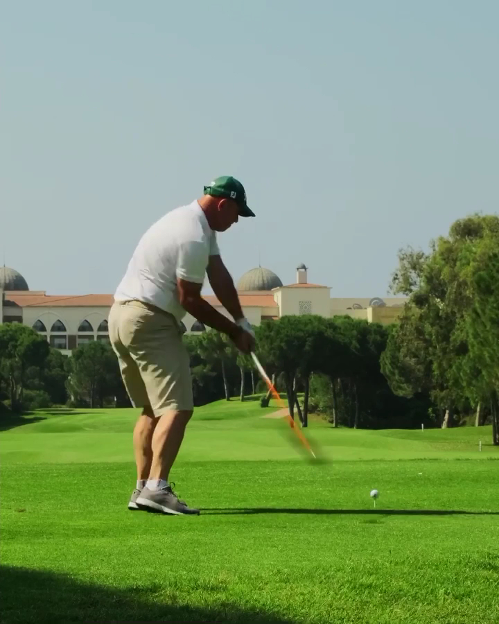 Vīrietis spēlē golfu Kempinski Hotel The Dome golfa laukumā Belekā — fonā redzama viesnīcas ēka ar kupoliem