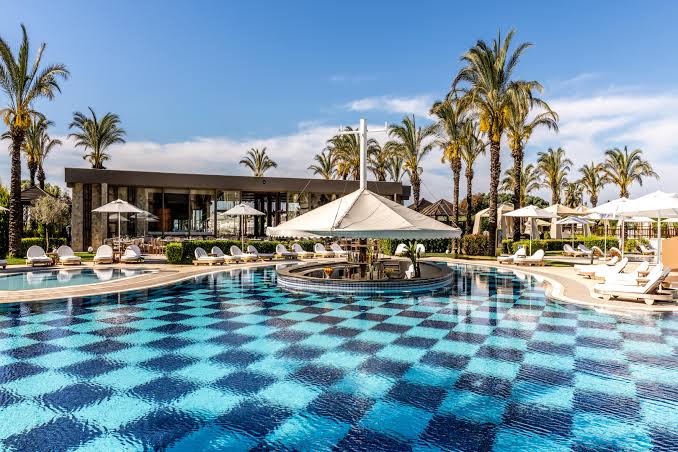 Kempinski Hotel The Dome galvenais baseins ar šaha raksta flīzēm, bāru ūdenī un saulessargiem Belekas piekrastē