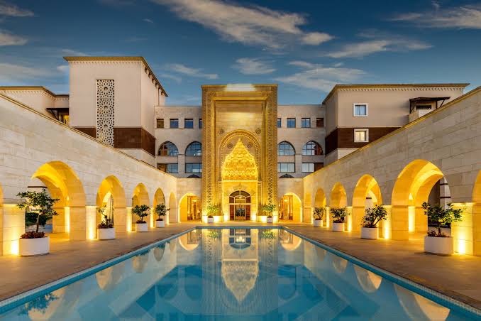 Kempinski Hotel The Dome iekšpagalms ar dekoratīvu baseinu, arkādēm un izgaismotu zelta kupolu vakara stundā Belekā.