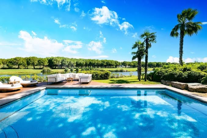Kempinski Hotel The Dome āra baseins ar atpūtas zonu, dīvāniem un palmām pie ezera un golfa laukuma Belekā