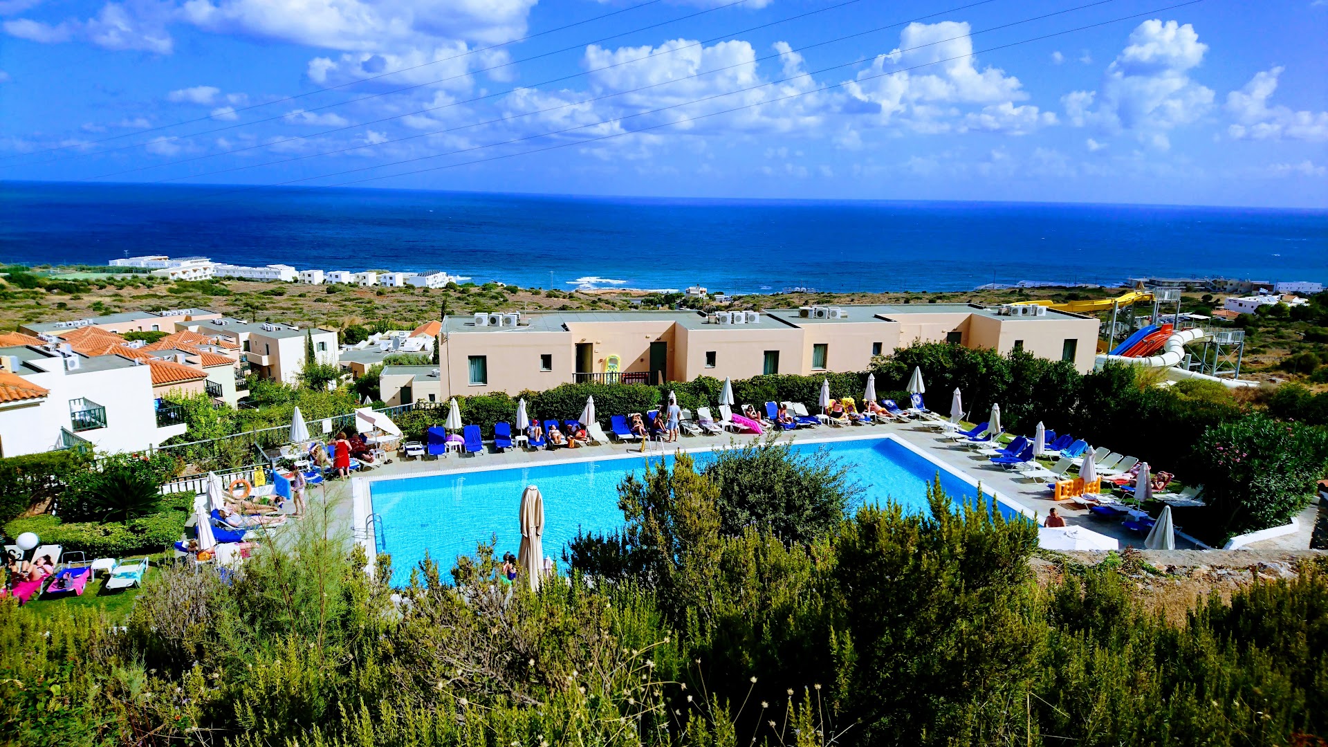Panorāmas skats uz Zeus Hotels The Village Resort & Waterpark baseinu, akvaparku un Vidusjūras piekrasti Hersonisā