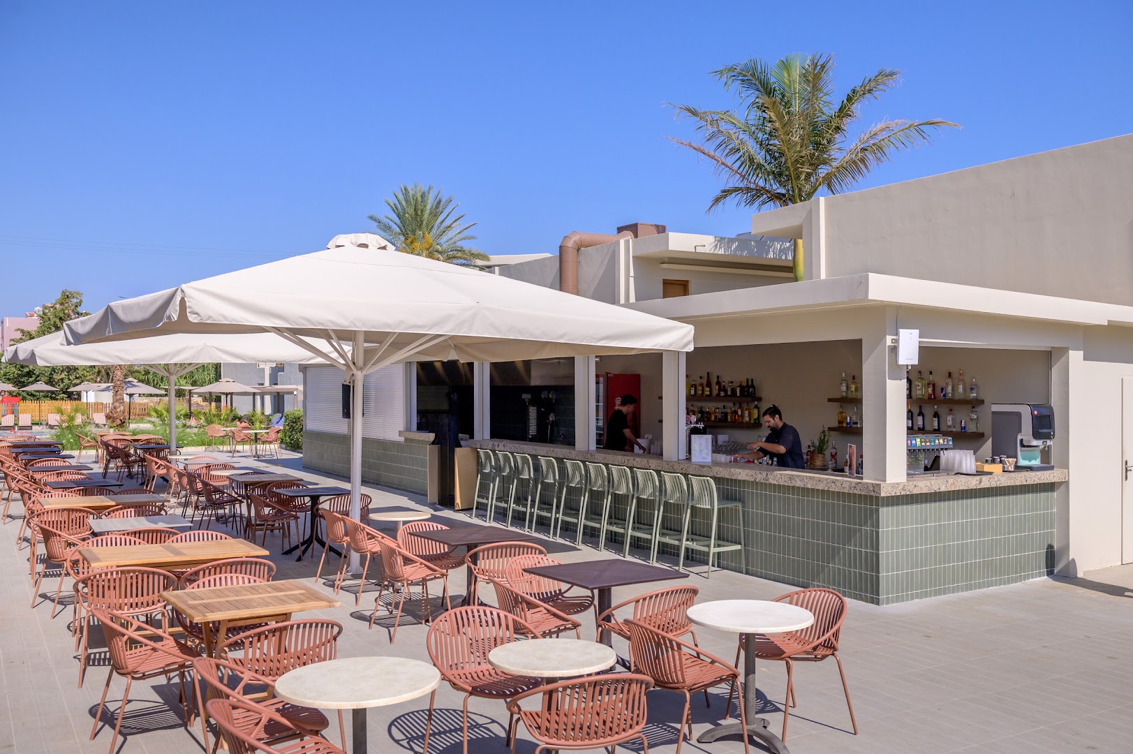 Zeus Hotels Ydoria Resort āra bārs pie baseina ar modernām mēbelēm, saulessargiem un palmām fonā zem skaidrām debesīm
