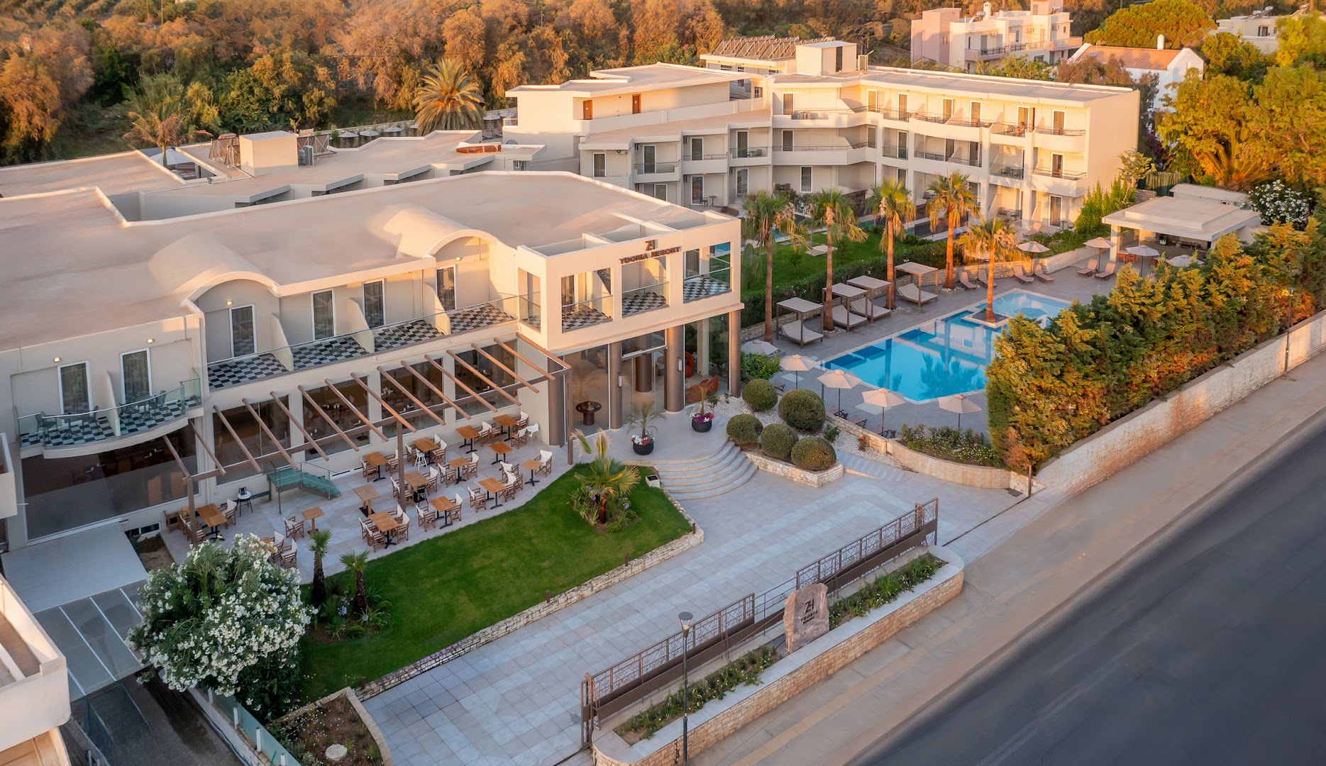 Ydoria Resort modernā arhitektūra ar āra terasi, restorāna zonu un zilu peldbaseinu palmu ieskautā teritorijā dienas gaismā