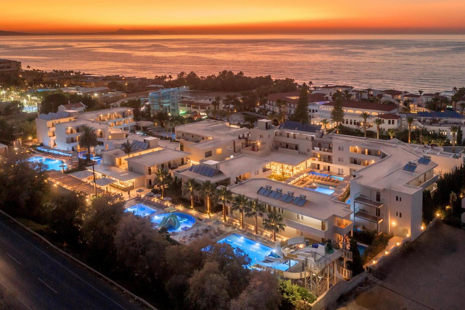 Zeus Hotels Ydoria Resort skats no putna lidojuma saulrietā — izgaismoti baseini, viesnīcas korpusi un jūra fonā Stalidā, Krētā