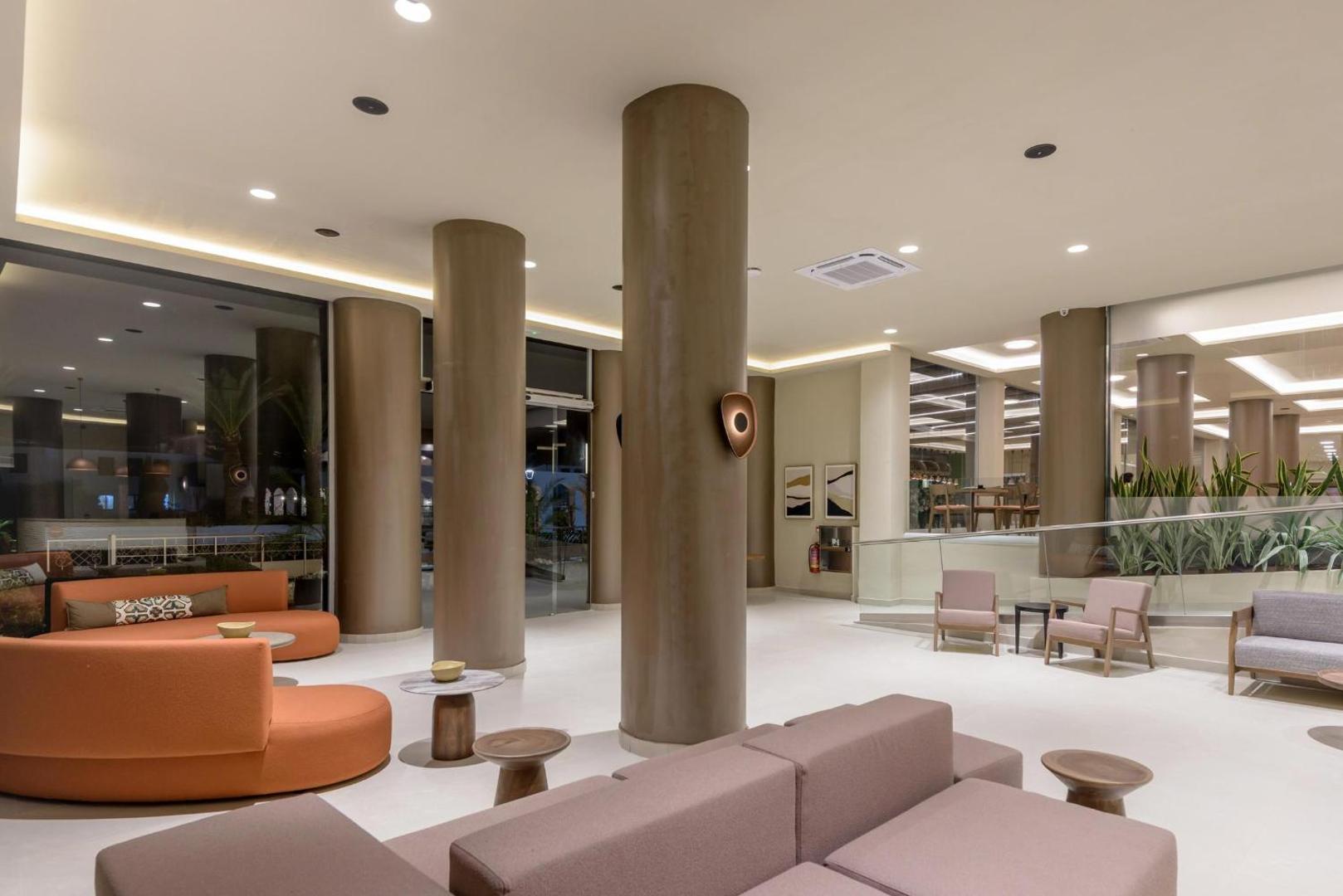 Zeus Hotels Ydoria Resort lobby atpūtas zona ar ērtiem dīvāniem, dizaina mēbelēm un plašiem logiem nakts noskaņās