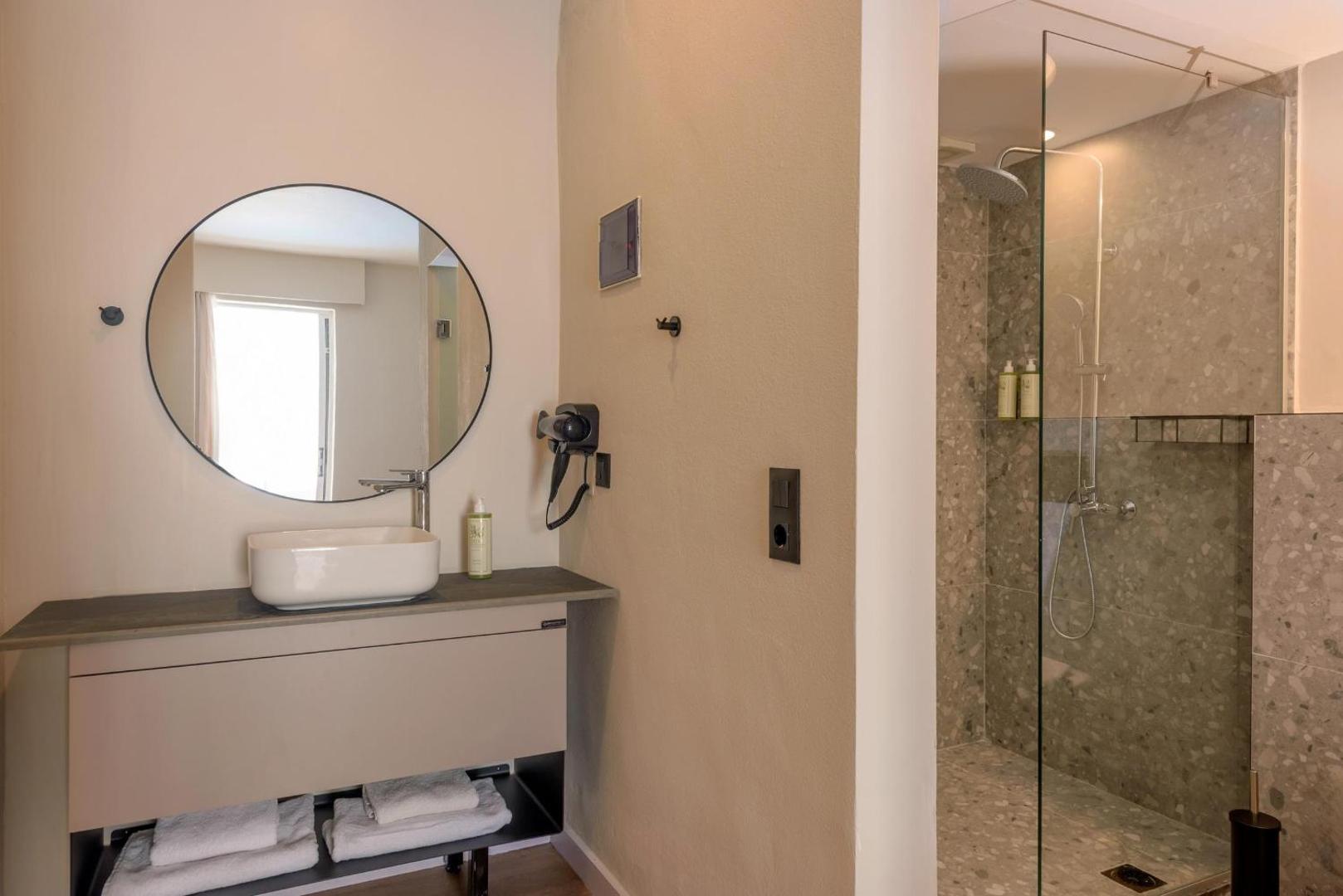 Zeus Hotels Ydoria Resort numura vannas istaba ar apaļu spoguli, izlietni un atsevišķu dušas zonu gaišos toņos