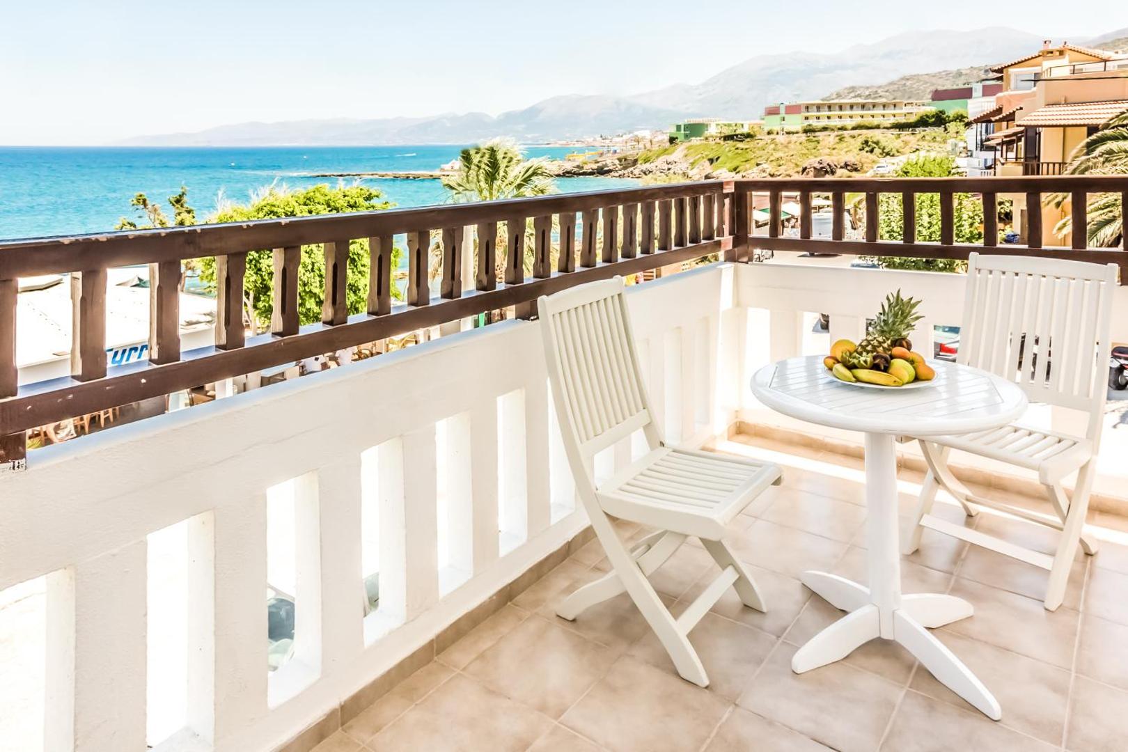 Porto Greco Village plašā terase ar baltām mēbelēm un panorāmas skatu uz Krētas piekrasti un kalniem
