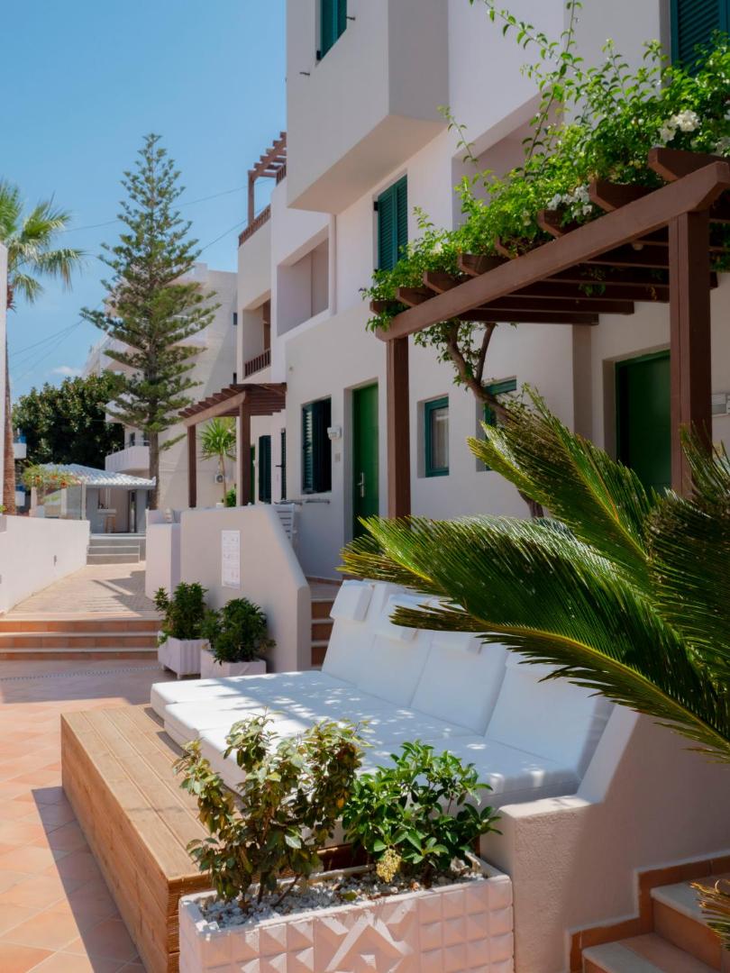 Porto Greco Village numuru korpusa pagalms ar baltu dīvānu atpūtai, koka detaļām un zaļojošiem augiem saulainā dienā