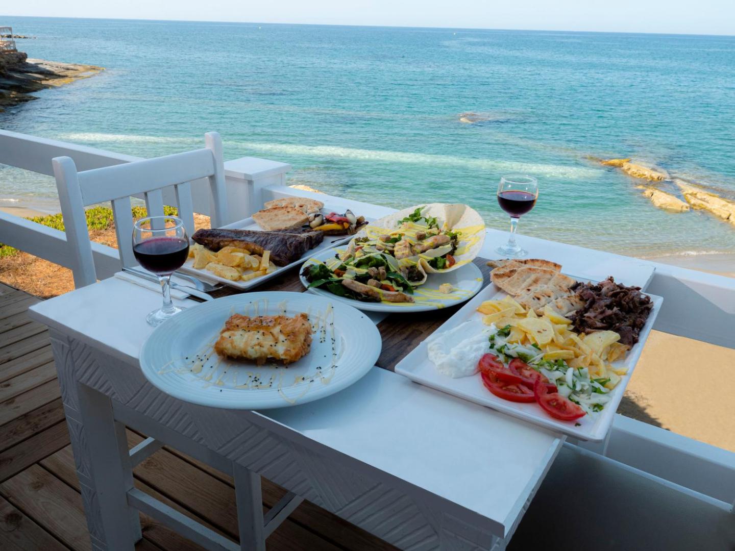 Porto Greco Village restorāna galds ar grieķu virtuves ēdieniem un vīnu uz terases ar skatu uz Vidusjūru Hersonisā, Krētā
