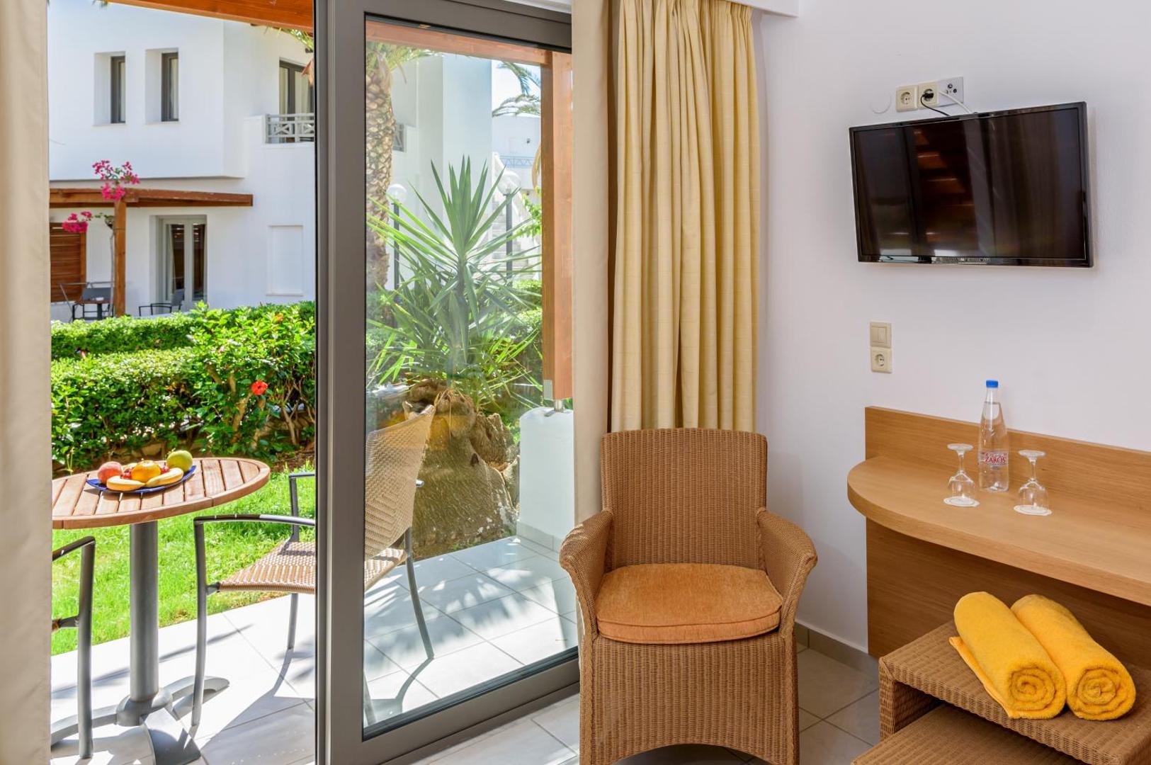Skats no Annabelle Beach Resort numura iekšpuses uz saulaino terasi, kur redzams galds ar augļiem un viesnīcas teritorijas apstādījumi.