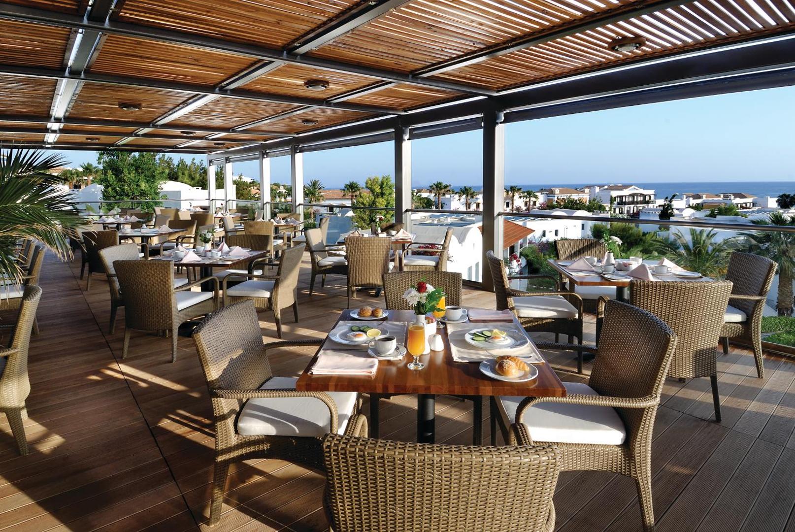 Annabelle Beach Resort āra terases restorāns ar koka nojumi, pītiem krēsliem un skatu uz jūru un kūrorta ēkām