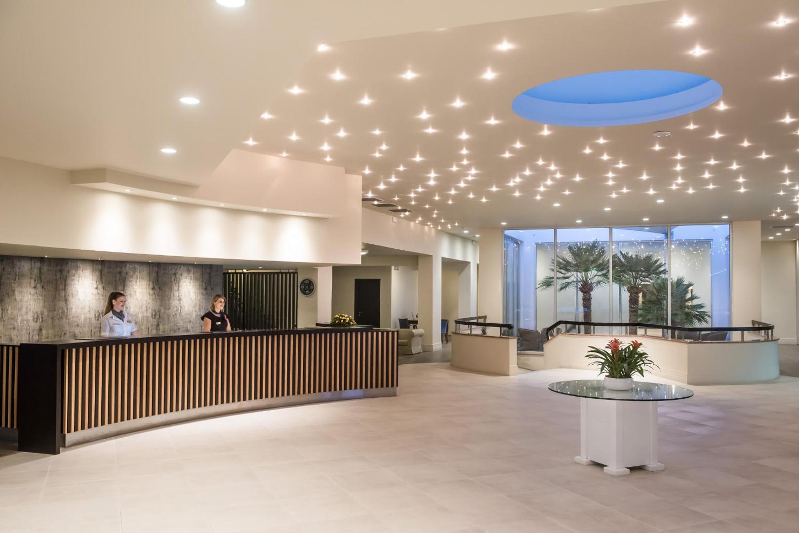 Annabelle Beach Resort plašais un gaišais vestibils ar modernu recepcijas leti, dekoratīvu apgaismojumu un palmu skatu pa logu