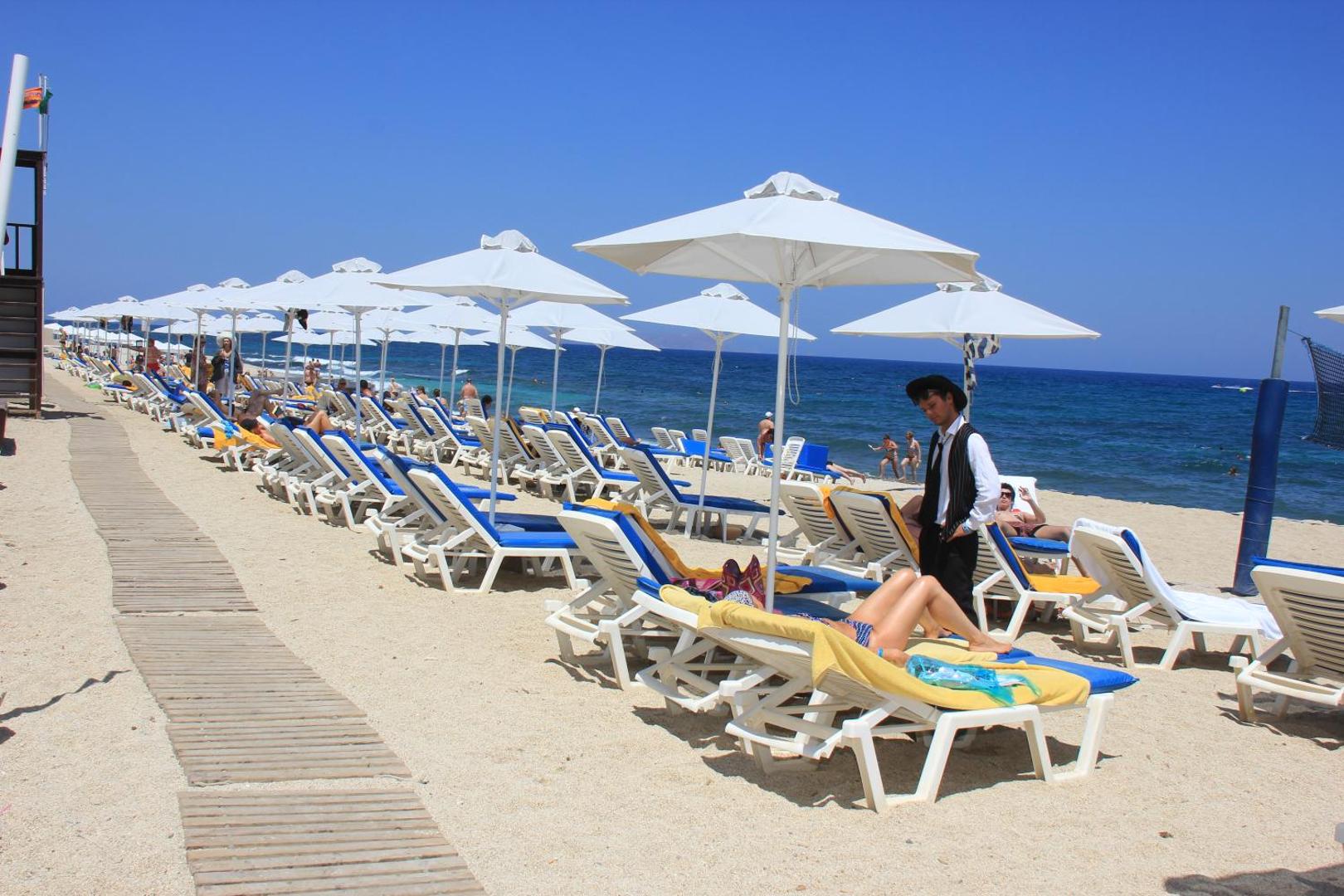 Annabelle Beach Resort labiekārtota pludmale ar baltiem saulessargiem, sauļošanās krēsliem un viesmīli, kas apkalpo viesus pie jūras