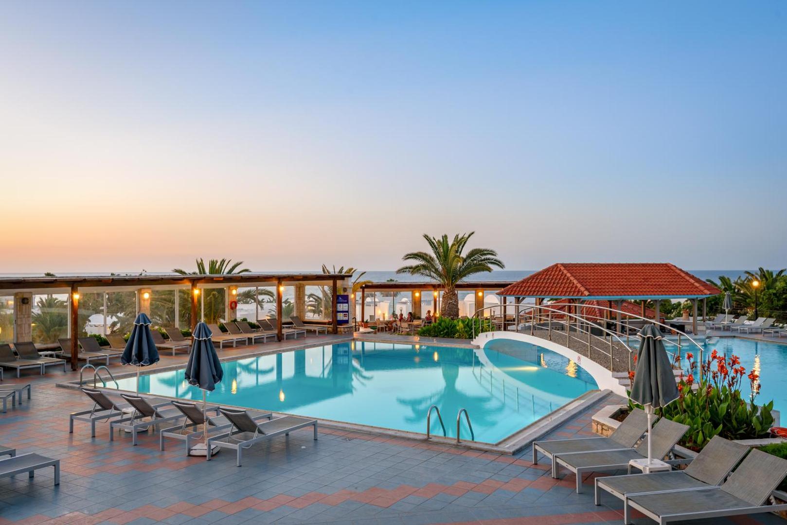 Annabelle Beach Resort baseins ar tiltiņu un atpūtas krēsliem vakara stundā — skats uz jūru un kūrorta arhitektūru