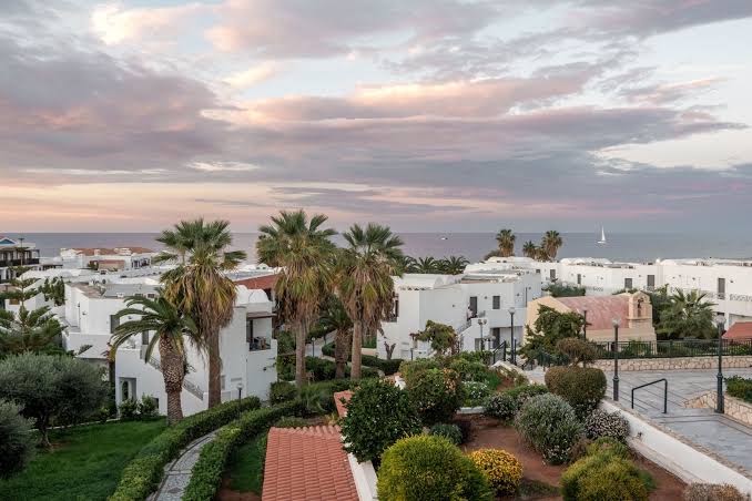 Annabelle Beach Resort skats no augšas uz viesnīcas teritoriju, baltajām ēkām un palmām Hersonisā, Krētā saulrieta laikā
