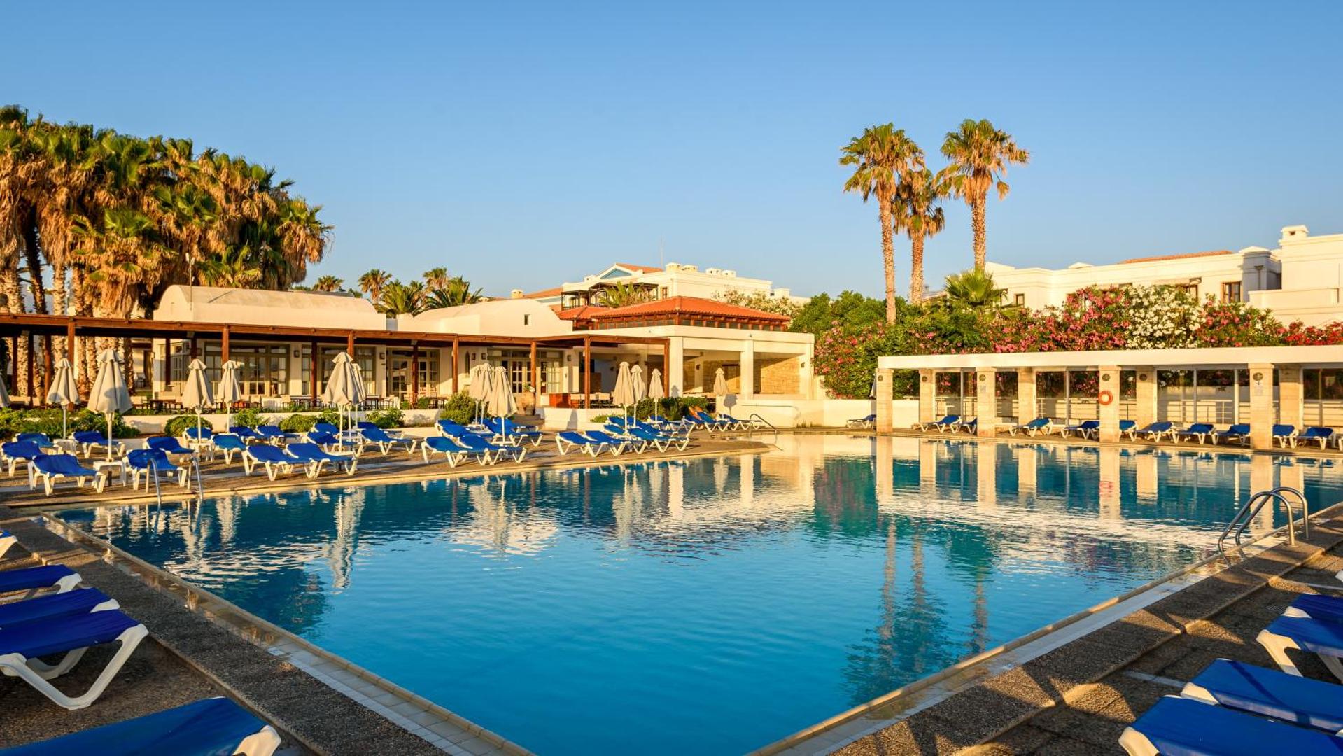 Annabelle Beach Resort plašais peldbaseins pie viesnīcas bungalo tipa ēkām — zili sauļošanās krēsli un palmas dienas saulē