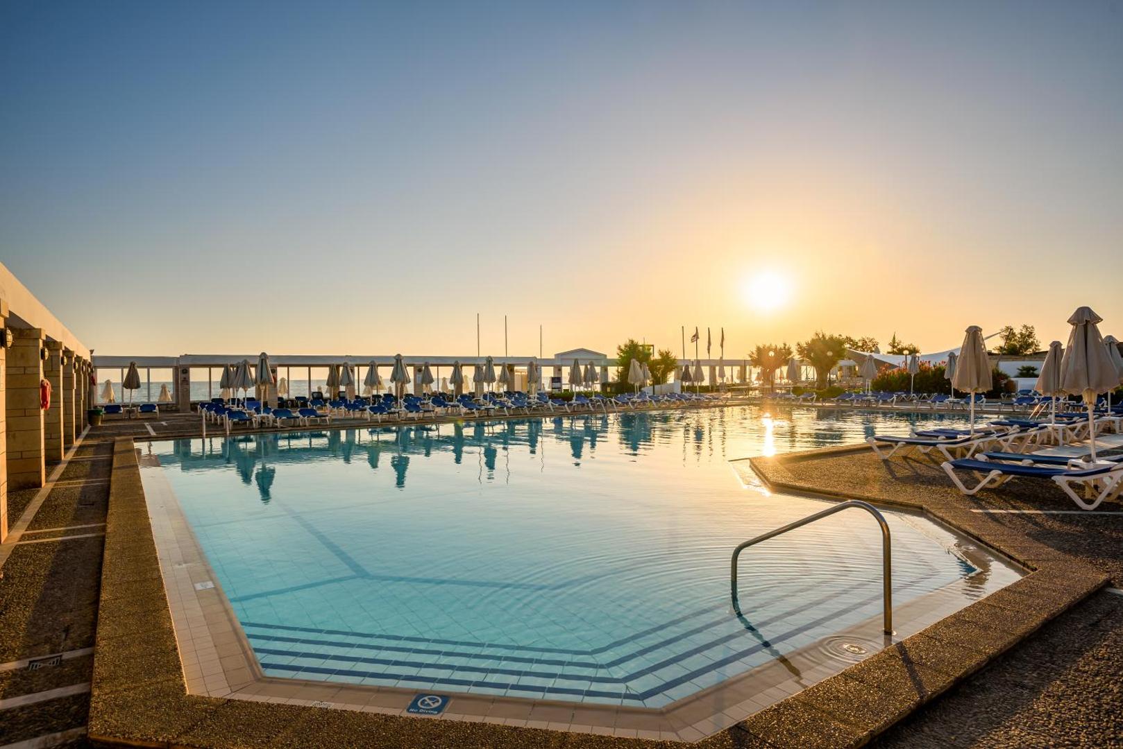 Annabelle Beach Resort galvenais āra baseins saulrietā Hersonisā, Krētā — plaša atpūtas zona ar sauļošanās krēsliem un saulessargiem pie jūras