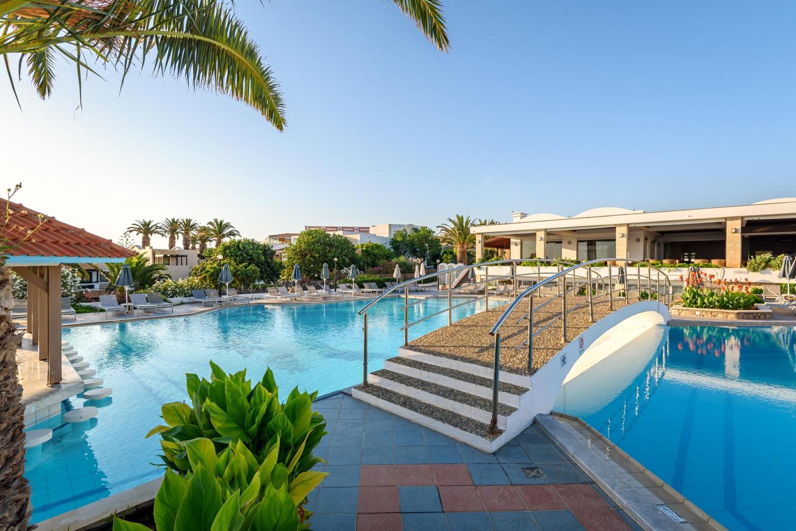 Annabelle Beach Resort dārza baseins ar dekoratīvu tiltiņu un palmām — gaiša un plaša atpūtas zona pie viesnīcas galvenās ēkas